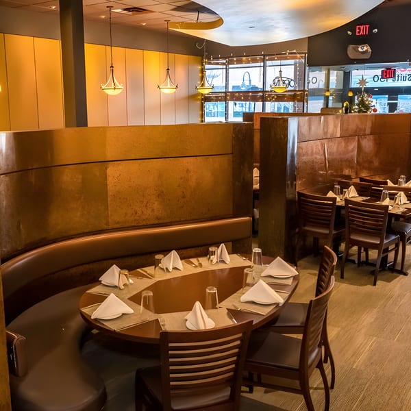 Warmly lit Indian restaurant interior with a large curved booth and set tables, ready for diners.