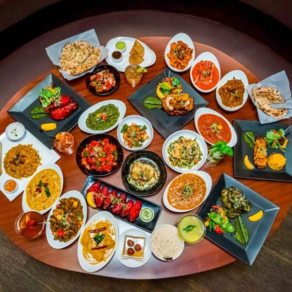 A large spread of various Indian dishes, including curries, rice, naan, and grilled meats, on a round table.