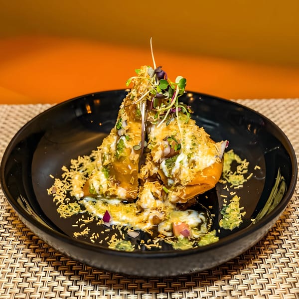 Aditi Indian Dining's samosa chaat, topped with sauces, microgreens, and crunchy sev, on a black plate.