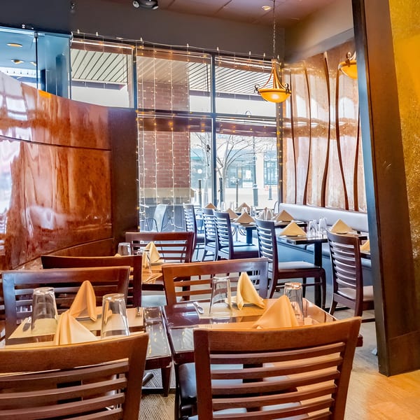 Interior of Aditi Indian Dining, showing set tables, wooden chairs, and large windows with string lights.