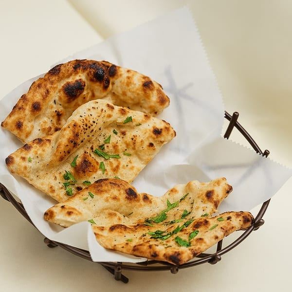 Three pieces of golden-brown naan bread, garnished with fresh herbs, in a dark wire basket.