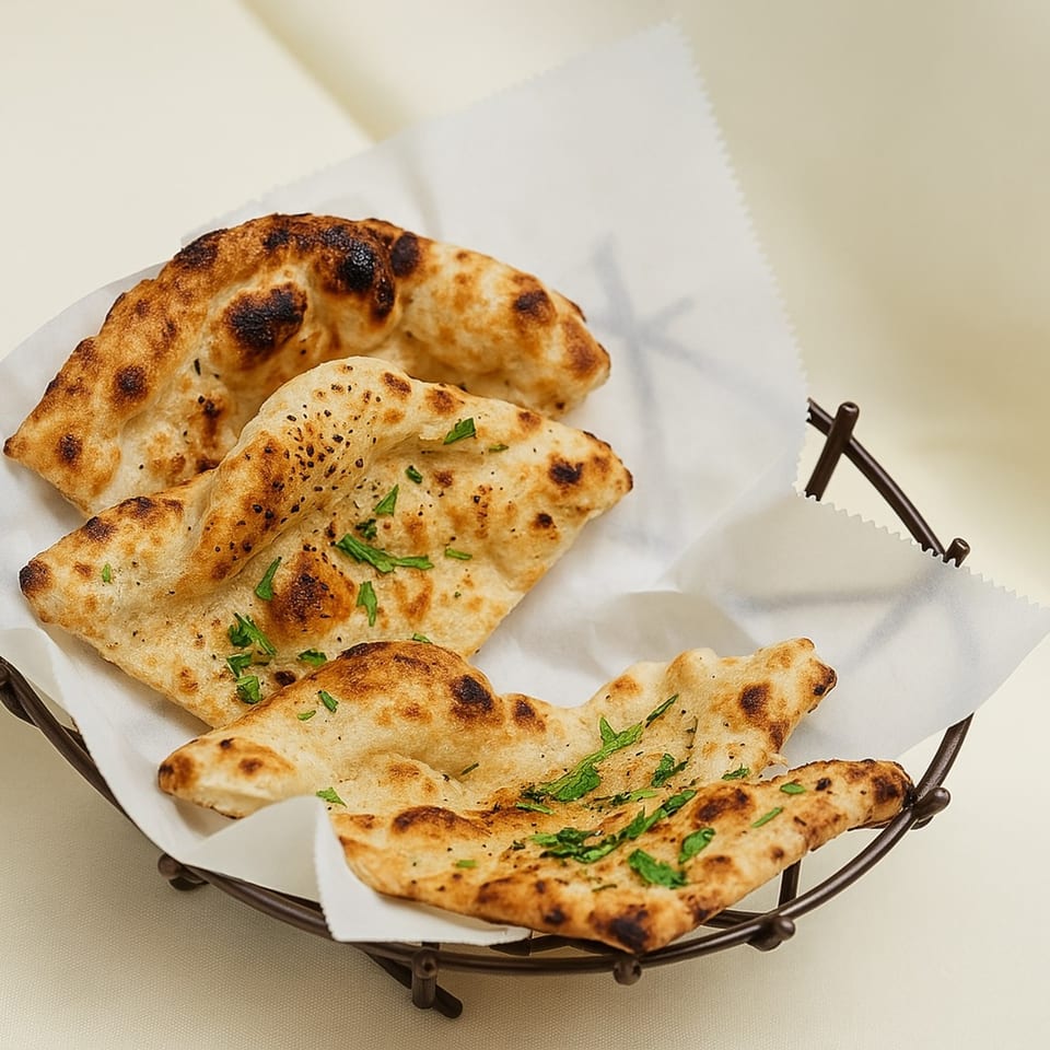Three pieces of golden-brown naan bread, garnished with fresh herbs, in a dark wire basket.