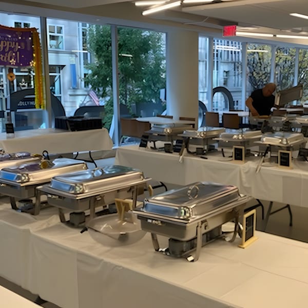 A buffet line with multiple chafing dishes on white-covered tables, with a person in the background.