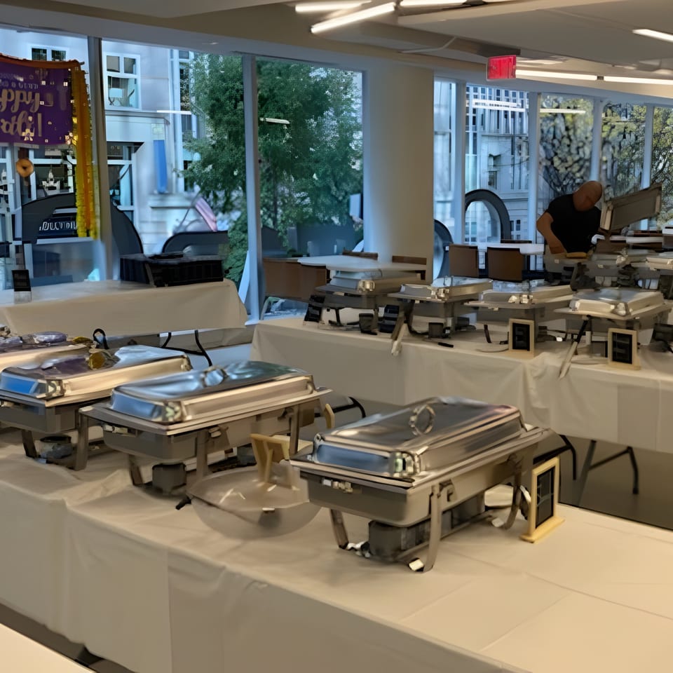 A buffet line with multiple chafing dishes on white-covered tables, with a person in the background.