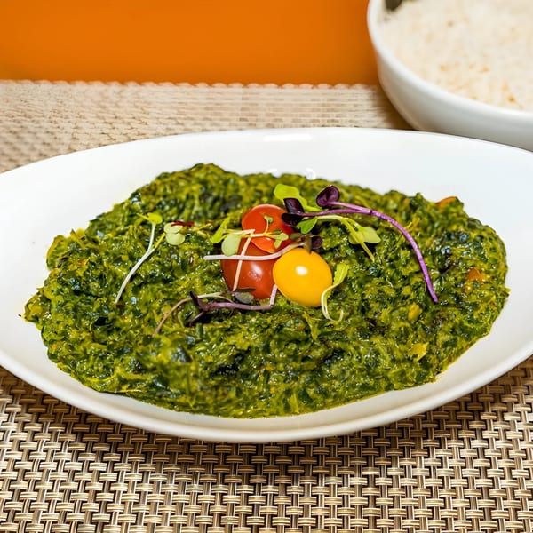 Aditi Indian Dining's vibrant green spinach dish, garnished with cherry tomatoes and microgreens, with rice in the background.