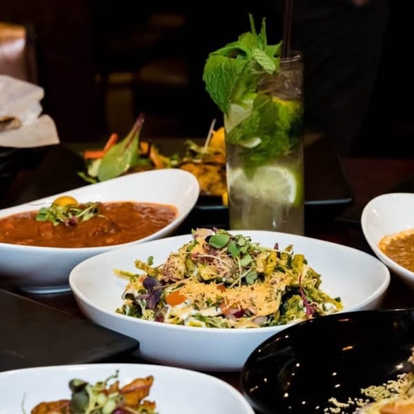Aditi Indian Dining dishes: a mojito, a curry, and two salads, one topped with crispy noodles.