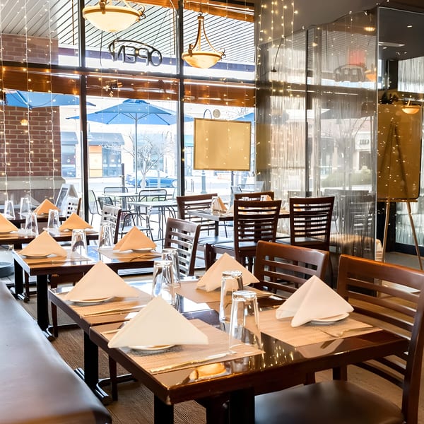 Aditi Indian Dining interior with set tables, dark wood chairs, and large windows looking outside.